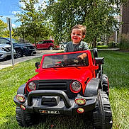 Marcelo joined the competition — help win amazing prizes! child, toddler, toy_car, red, grass, outdoor, sunny, smiling, greenery, tree, suburban, car, vehicle, play, fun, daytime, happy, person, jeep, sidewalk