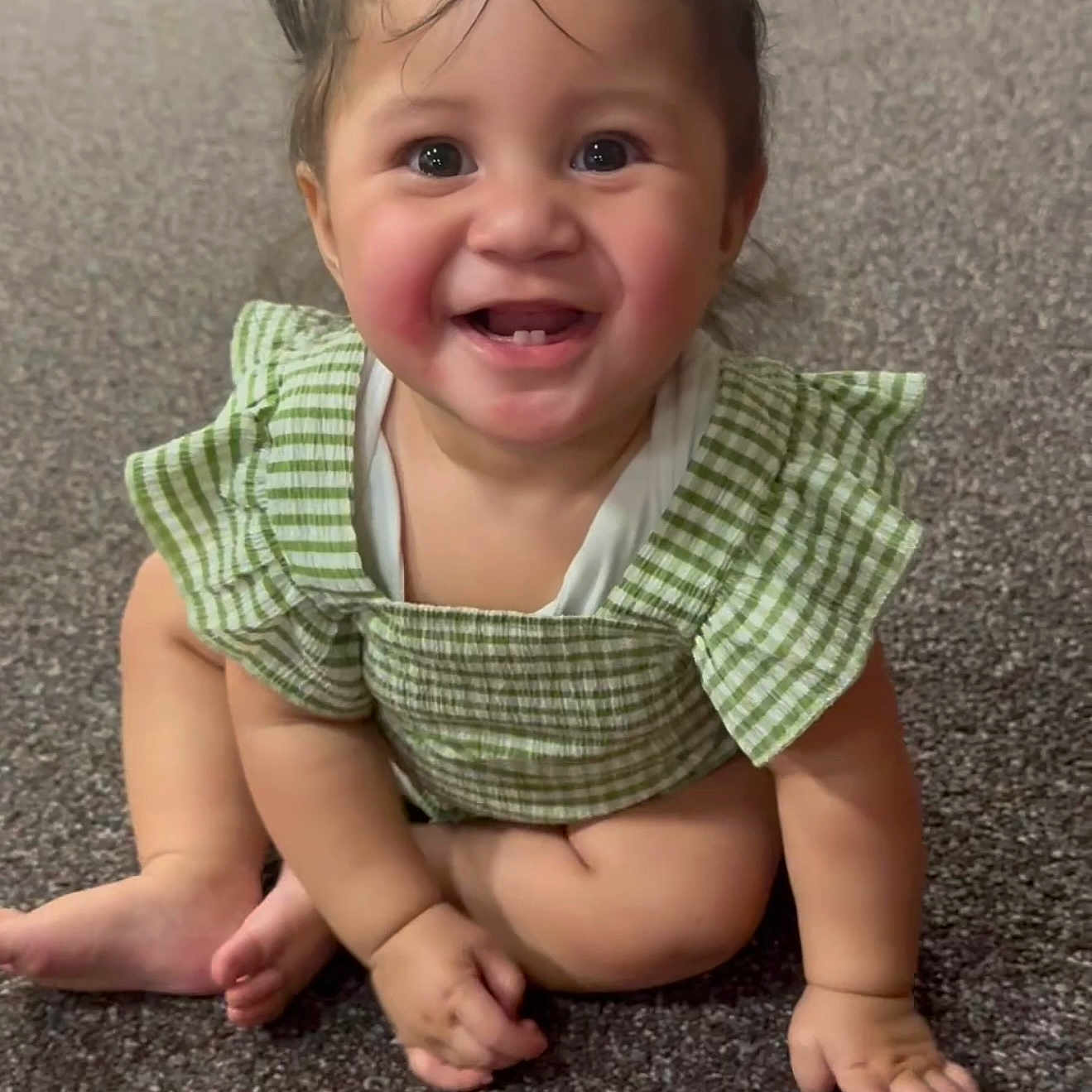 Lesieli is registered to the contest to win money with this photo: adorable, baby, blue_flower_clips, carpet, checkered, child, cute, eyes, face, feet, green_outfit, hands, happy, indoors, infant, pigtails, portrait, sitting, smiling, tooth