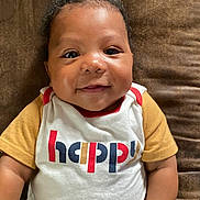 Josyah is registered to the contest to win money with this photo: baby, brown_background, casual, child, closeup, clothing, cute, expression, face, happy, human, infant, joyful, lying_down, mustard_sleeves, portrait, smiling, toddler, white_shirt, young