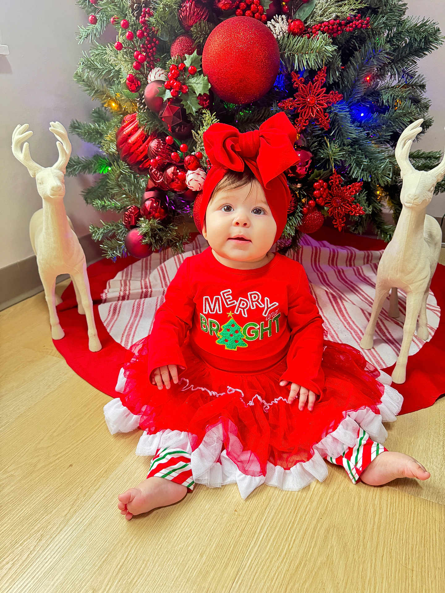 Thaizary joined the competition — help win amazing prizes! baby, child, christmas_tree, holiday, red_clothing, headband, bow, reindeer_statue, floor, festive, decoration, ornaments, tulle_skirt, striped_pants, indoors, smiling, cute, celebration, seasonal, happy