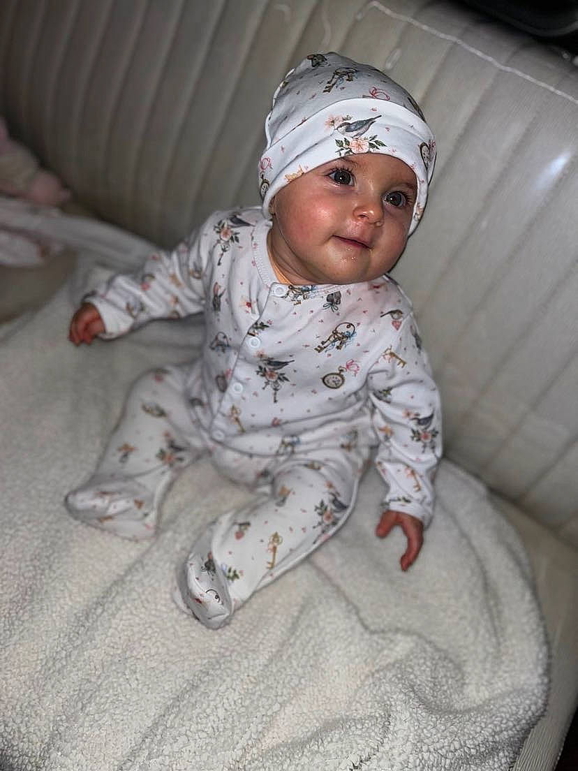 Iris a rejoint le concours — aidez-le/la à gagner de superbes lots ! baby, baby_toddler_clothing, beanie, cap, carmine, child, comfort, face, flooring, fun, fur, head, headwear, linens, pattern, person, personal_protective_equipment, portrait_photography, room, sitting