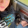 Simba is registered to the contest to win money with this photo: person, cat, kitten, lap, car_interior, jeans, black_tshirt, seat, window, daylight, relaxing, closeup, hair, hand, feline, pet, casual, resting, sunlight, travel