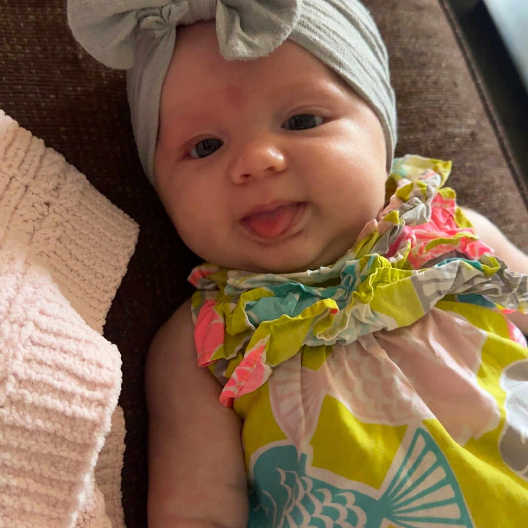 Nova joined the competition — help win amazing prizes! baby, blanket, bow, child, colorful_clothing, couch, cute, dress, fish_pattern, headband, indoor, infant, lying_down, person, playful, portrait, relaxed, smiling, soft_texture, tongue