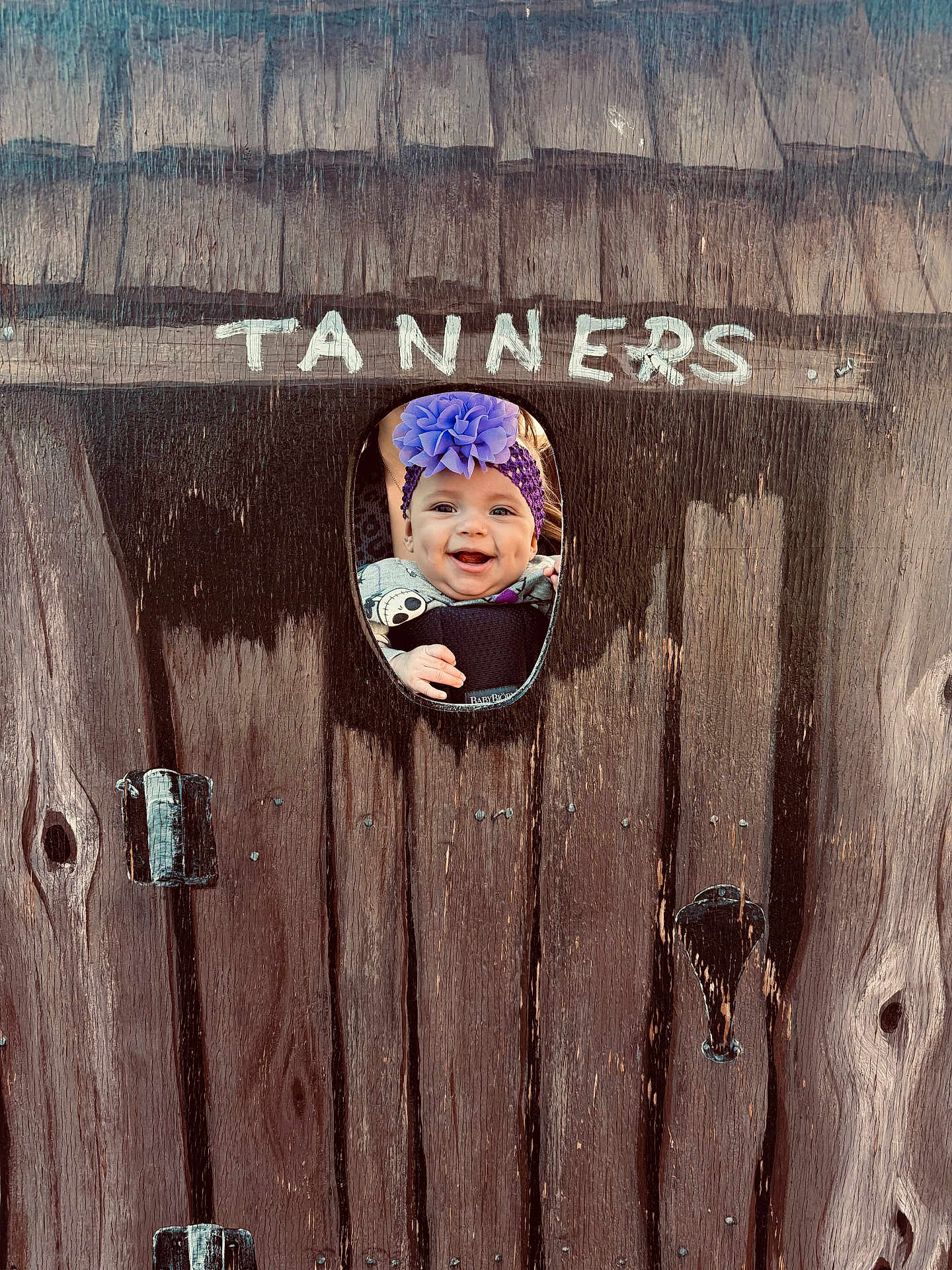 Cali joined the competition — help win amazing prizes! baby, child, face, smile, headband, flower, wood, fence, cutout, happy, outdoor, person, infant, purple, clothing, portrait, cute, wooden_fence, baby_carrier, peeking
