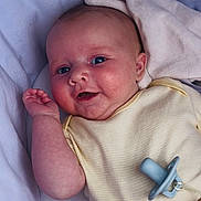 Tilly joined the competition — help win amazing prizes! baby, infant, smile, face, hand, blanket, pacifier, clothing, beads, name_tag, cute, lying_down, soft_texture, happy, skin, blue_eyes, yellow_outfit, closeup, indoors, child
