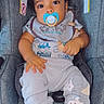 Prince is registered to the contest to win money with this photo: baby, child, car_seat, pacifier, bib, curly_hair, clothing, pants, elephant_design, socks, infant, indoor, cute, comfort, seat, portrait, young_child, holding, looking_up, soft_lighting