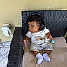 Prince is registered to the contest to win money with this photo: baby, child, headphones, pacifier, toy, wicker_chair, cushion, socks, curly_hair, outdoor, floor_tiles, wall, clothing, seated, looking_away, infant, cute, relaxed, casual, furniture