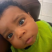 Prince joined the competition — help win amazing prizes! baby, child, face, curious, closeup, green_bib, clothing, indoor, person, expression, head, skin, hair, seat, chair, tile_floor, portrait, young, infant, looking