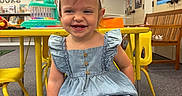 Scarlett Drew is registered to the contest to win money with this photo: child, toddler, smiling, headband, denim, romper, yellow_chair, classroom, toys, educational_posters, carpet, bench, table, happy, indoor, person, furniture, playroom, cute, kid