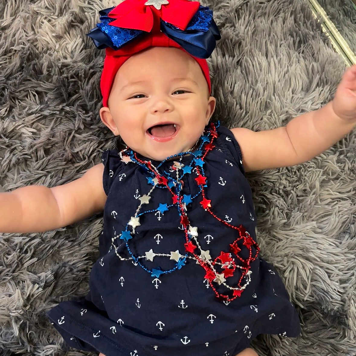 Valentina Jade. is registered to the contest to win money with this photo: anchors, baby, blue, bow, child, cute, dress, fluffy, happy, headband, indoors, infant, lying_down, navy_blue, necklaces, person, red, rug, smiling, stars