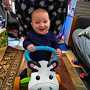 Ezékiel a rejoint le concours — aidez-le/la à gagner de superbes lots ! baby, carpet, child, colorful, couch, floor, footwear, furniture, hand, happy, indoor, living_room, pattern, person, play, shorts, smiling, toy, walker, window