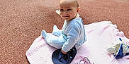 Ezékiel participe au concours pour gagner de l'argent avec cette photo : baby, blanket, cap, casual_clothing, child, cute, daylight, fish_toy, happy, infant, outdoor, park, play, playground, recreation, rubber_floor, sitting, smiling, spring_rider, toy