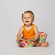 Lilah joined the competition — help win amazing prizes! baby, child, toddler, portrait, smiling, happy, sitting, orange_shirt, floral_skirt, hair_bow, blonde_hair, barefoot, studio, white_background, colorful, fashion, infant, face, indoor, photography