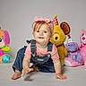 Lilah is registered to the contest to win money with this photo: baby, child, infant, smiling, portrait, sitting, party_hat, stuffed_animals, plush_toys, teddy_bear, colorful, birthday, headband, bow, overalls, pink_shirt, indoor, studio, white_background, photography