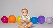 Lilah is registered to the contest to win money with this photo: baby, child, toddler, smiling, sitting, portrait, indoor, studio, balloons, colorful, rainbow, red_balloon, orange_balloon, yellow_balloon, blue_balloon, purple_balloon, striped_clothing, hair_bow, barefoot, happy