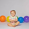 baby, child, toddler, smiling, sitting, portrait, indoor, studio, balloons, colorful, rainbow, red_balloon, orange_balloon, yellow_balloon, blue_balloon, purple_balloon, striped_clothing, hair_bow, barefoot, happy