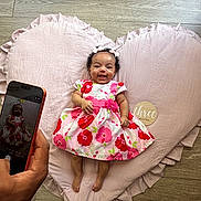 Aracelis joined the competition — help win amazing prizes! baby, infant, smile, dress, floral, heart_shaped_pillow, pink, floor, wood, hand, smartphone, photography, happy, child, cute, portrait, indoors, ribbon, headband, three_months