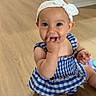 Camila is registered to the contest to win money with this photo: baby, blue_dress, bow, checkered, child, cute, fingers_in_mouth, floor, girl, happy, headband, indoors, infant, person, playful, sitting, smiling, toddler, wooden_floor, young_child