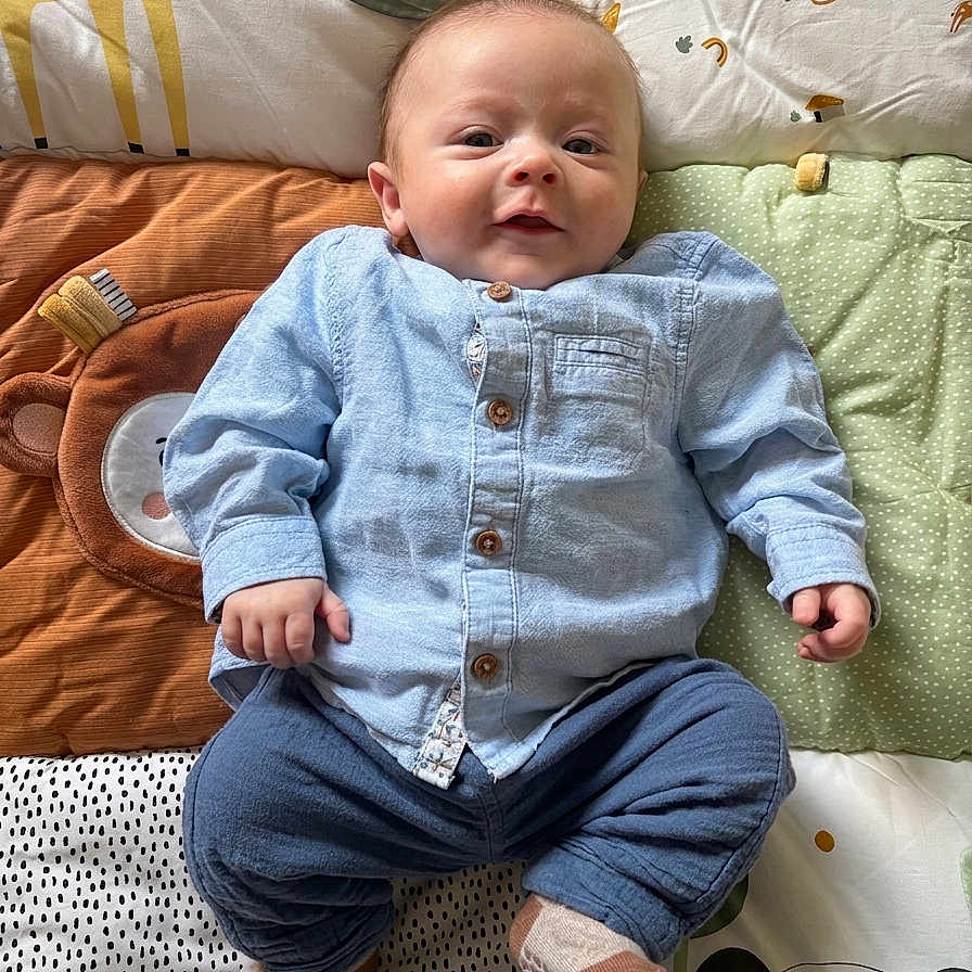Malo participe au concours pour gagner de l'argent avec cette photo : baby, infant, child, blue_shirt, pants, socks, lying_down, patterned_quilt, giraffe, monkey, panda, animal_print, cute, smiling, indoor, soft_toys, colorful, portrait, face, happy