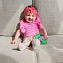 baby, baby_clothes, beige_couch, child, colorful_toy, couch, cute, feet, happy, headwear, indoor, infant, legs, pink_headband, pink_top, playful, sitting, smiling, soft_lighting, toy