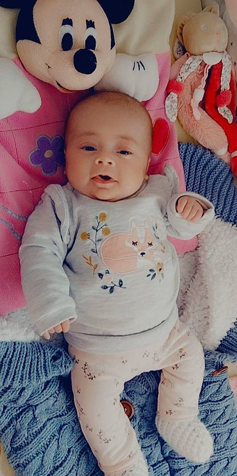 Léane participe au concours pour gagner de l'argent avec cette photo : arm, baby, baby_toddler_clothing, cheek, eye, face, facial_expression, hand, happy, head, iris, lip, person, pink, product, skin, sleeve, smile, standing, textile