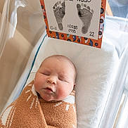 Oakland is registered to the contest to win money with this photo: newborn, baby, infant, sleeping, blanket, hospital_bassinet, footprints, card, cozy, wrapped, bed, cute, peaceful, child, person, indoors, soft, hospital, portrait, resting
