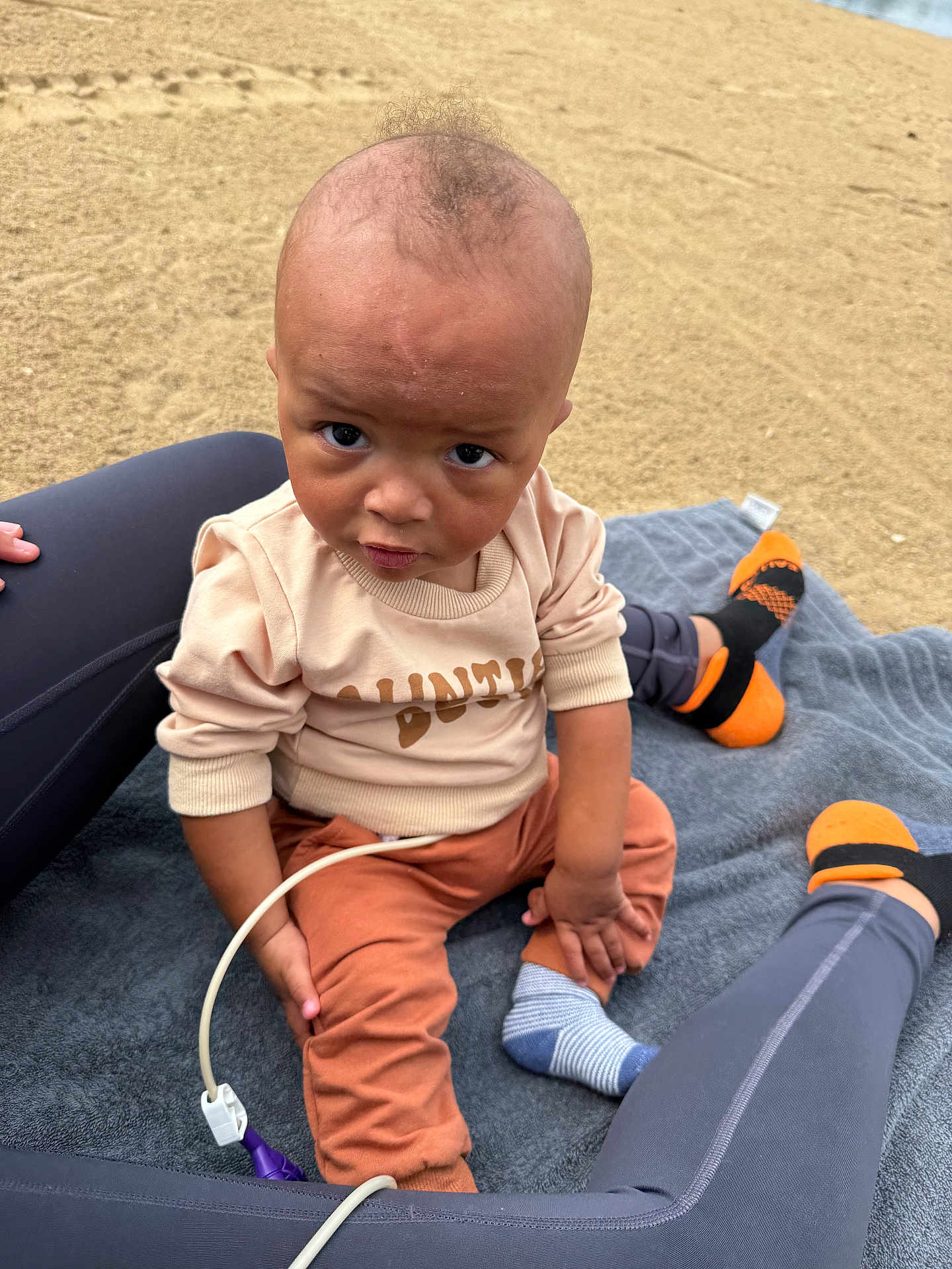 Amari is registered to the contest to win money with this photo: toddler, child, beach, sand, blanket, sitting, clothing, socks, legs, person, outdoor, casual, expression, curious, sweater, pants, baby, footwear, skin, head
