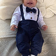 Yumel is registered to the contest to win money with this photo: baby, smiling, bow_tie, suspenders, white_shirt, pants, socks, blanket, couch, happy, child, portrait, indoor, cute, infant, clothing, face, hands, feet, lying_down