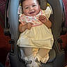 baby, child, car_seat, smiling, curly_hair, bib, white_dress, socks, indoor, happy, person, cute, infant, seat, clothing, footwear, toddler, car_safety, skin, portrait