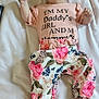 baby, child, infant, bed, bedding, headband, floral, pants, shirt, text, person, lying_down, cute, pink, flower, pattern, open_mouth, indoors, fabric, sleepwear