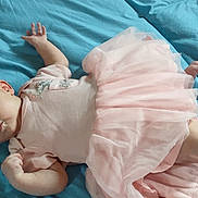 Makaylla is registered to the contest to win money with this photo: baby, infant, pink_dress, blue_bedspread, lying_down, cute, child, young, soft_fabric, clothing, bed, human, portrait, small_hands, small_feet, awake, indoors, resting, tulle_skirt, curious