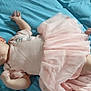 baby, infant, pink_dress, blue_bedspread, lying_down, cute, child, young, soft_fabric, clothing, bed, human, portrait, small_hands, small_feet, awake, indoors, resting, tulle_skirt, curious