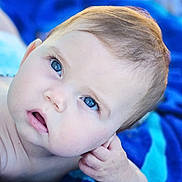 Iris participe au concours pour gagner de l'argent avec cette photo : baby, child, blue_eyes, close_up, curious, infant, looking_up, hand, face, skin, expression, blanket, soft_light, portrait, young, cute, innocence, outdoor, focus, head