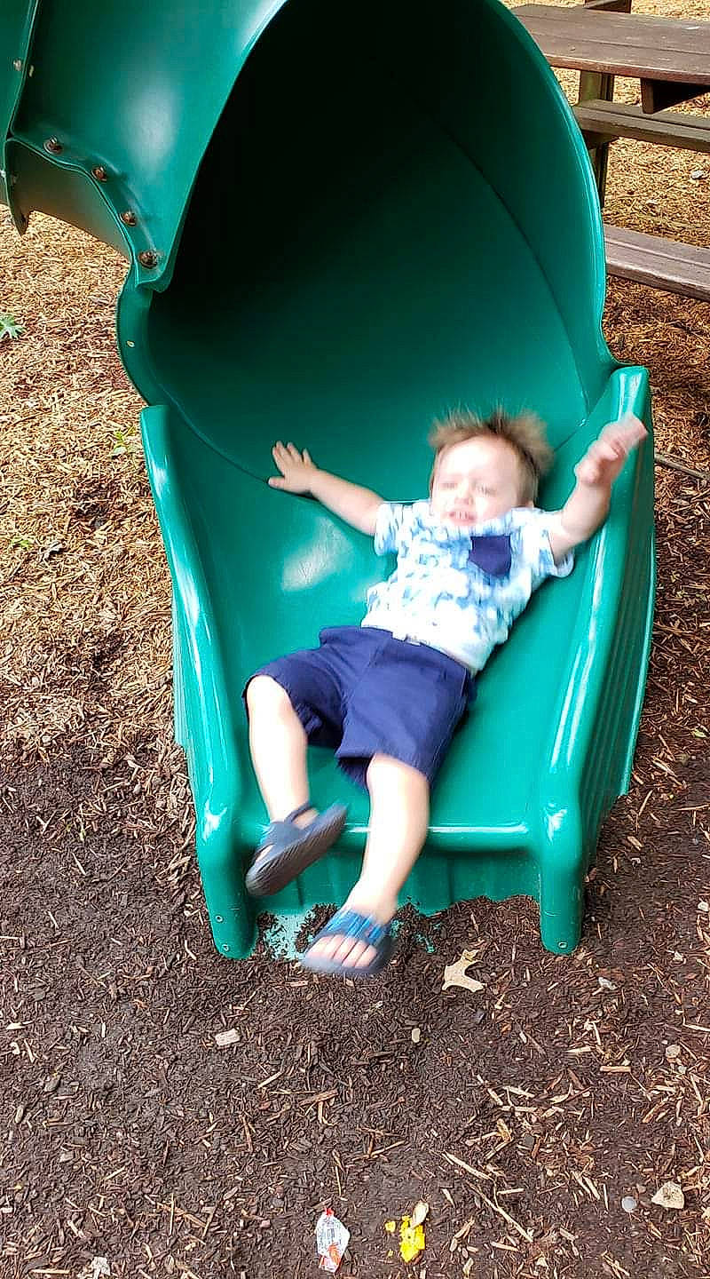 Deklan is registered to the contest to win money with this photo: child, chute, fun, grass, green, leisure, outdoor_play_equipment, person, play, playground, playground_slide, public_space, recreation, sitting, toddler, tree