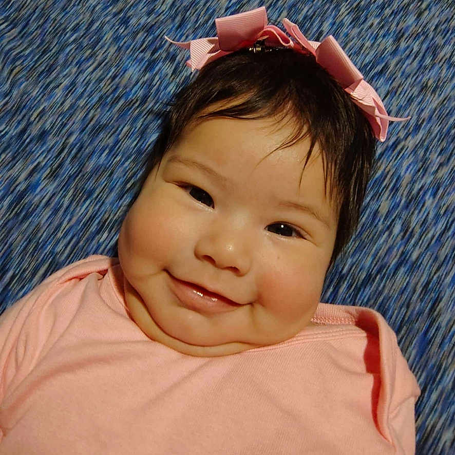 Daysha is registered to the contest to win money with this photo: baby, blue_background, cheeks, child, closeup, cute, face, hair, happy, headband, indoors, infant, lying_down, one_person, pink_bow, pink_clothing, portrait, skin, smile, young_child