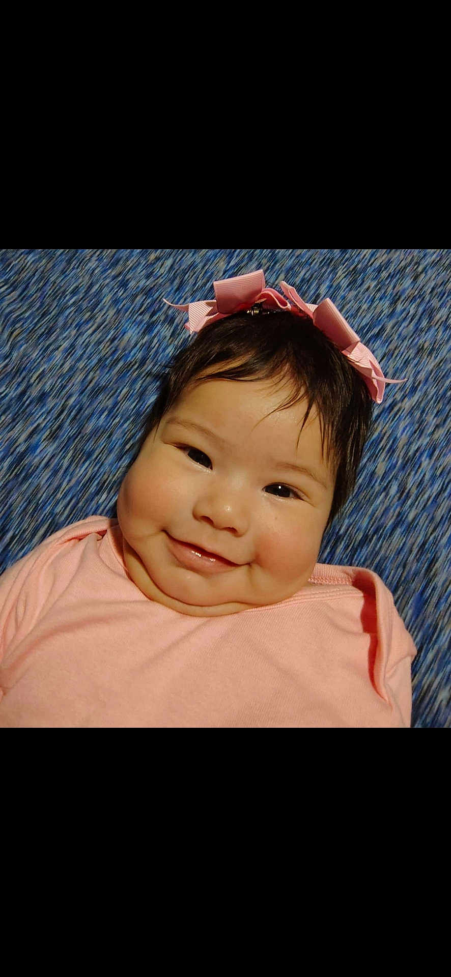 Daysha is registered to the contest to win money with this photo: baby, child, smile, pink_bow, pink_clothing, face, cheeks, hair, lying_down, blue_background, infant, cute, happy, portrait, headband, closeup, skin, young_child, one_person, indoors