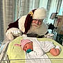 baby, newborn, hospital, incubator, santa_claus, pacifier, hat, blanket, white_clothing, glasses, beard, curtains, medical_equipment, smile, portrait, infant, holiday, christmas, person, gloves