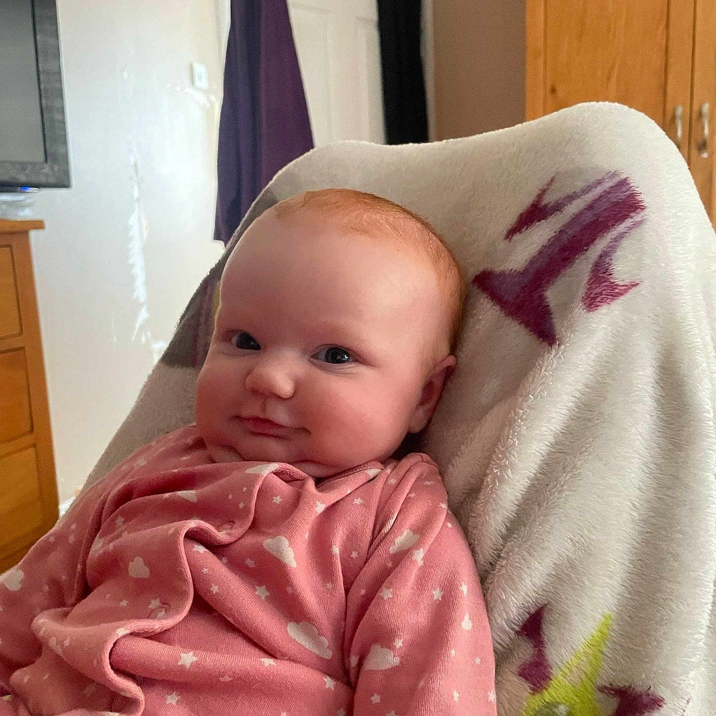 Elora is registered to the contest to win money with this photo: baby, blanket, child, cozy, curtain, cute, door, eyes, face, furniture, head, indoor, infant, pink_clothing, portrait, sleepwear, smile, soft_texture, warm, wooden_drawer