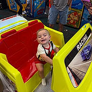 Noah joined the competition — help win amazing prizes! toddler, child, arcade, racing_car, smiling, indoor, game_machine, yellow, red, person, fun, play, joy, entertainment, family, toy, casual_clothing, happy, leisure, amusement