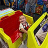 toddler, child, arcade, racing_car, smiling, indoor, game_machine, yellow, red, person, fun, play, joy, entertainment, family, toy, casual_clothing, happy, leisure, amusement