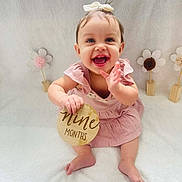 Meadow is registered to the contest to win money with this photo: baby, child, infant, girl, smiling, clapping, pink_dress, bow, wooden_sign, nine_months, sitting, white_blanket, decorations, flowers, happy, cute, portrait, indoors, soft_lighting, celebration
