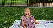 Lucia is registered to the contest to win money with this photo: baby, blanket, child, cute, daylight, fence, grass, happy, infant, lawn, nature, outdoor, park, people, playful, portrait, purple_dress, sitting, smiling, young