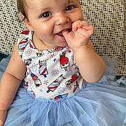 Luna is registered to the contest to win money with this photo: baby, child, smiling, blue_tutu, cute, sitting, thumb_in_mouth, colorful, rainbow_background, patterned_clothing, curly_hair, face, indoors, cushion, happy, portrait, playful, infant, apparel, person