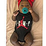 baby, infant, pacifier, headband, red_bow, onesie, black_clothing, lying_down, blanket, cute, child, adorable, infant_clothing, young_child, relaxed, indoors, soft_texture, skin, small_hands, small_feet