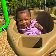 Paris joined the competition — help win amazing prizes! baby, child, toddler, swing, playground, outdoor, smiling, purple_dress, green_metal, trees, wood_chips, sunlight, park, fence, seat, infant, happy, cute, person, play