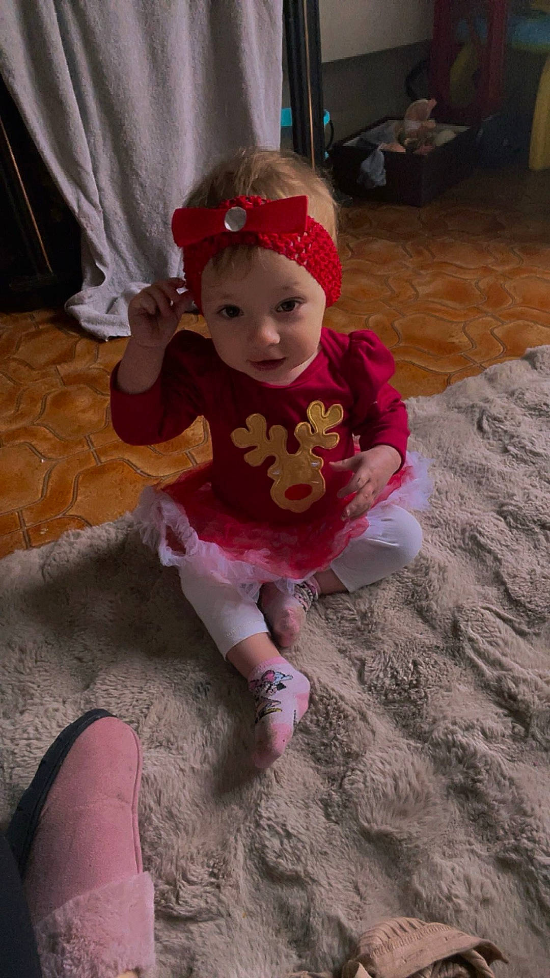 Yuna a rejoint le concours — aidez-le/la à gagner de superbes lots ! baby, casual, child, cozy, curious_expression, flooring, holiday_clothing, indoor, person, pink_socks, red_headband, red_outfit, reindeer_design, rug, sitting, slipper, soft_texture, toddler, toy_box, white_leggings