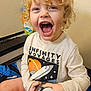 child, toddler, curly_hair, blond, smiling, laughing, open_mouth, teeth, eyes, graphic_tee, space_theme, spaceship, planet, shirt, holding, bottle, indoor, wall, diaper, person