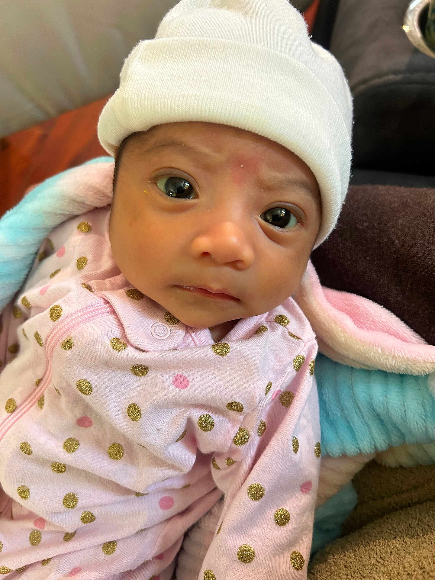 Gia S is registered to the contest to win money with this photo: baby, infant, face, hat, pink_clothing, polka_dots, blanket, indoor, curious_expression, newborn, closeup, person, soft_texture, cozy, child, cute, young, headwear, apparel, sleepwear