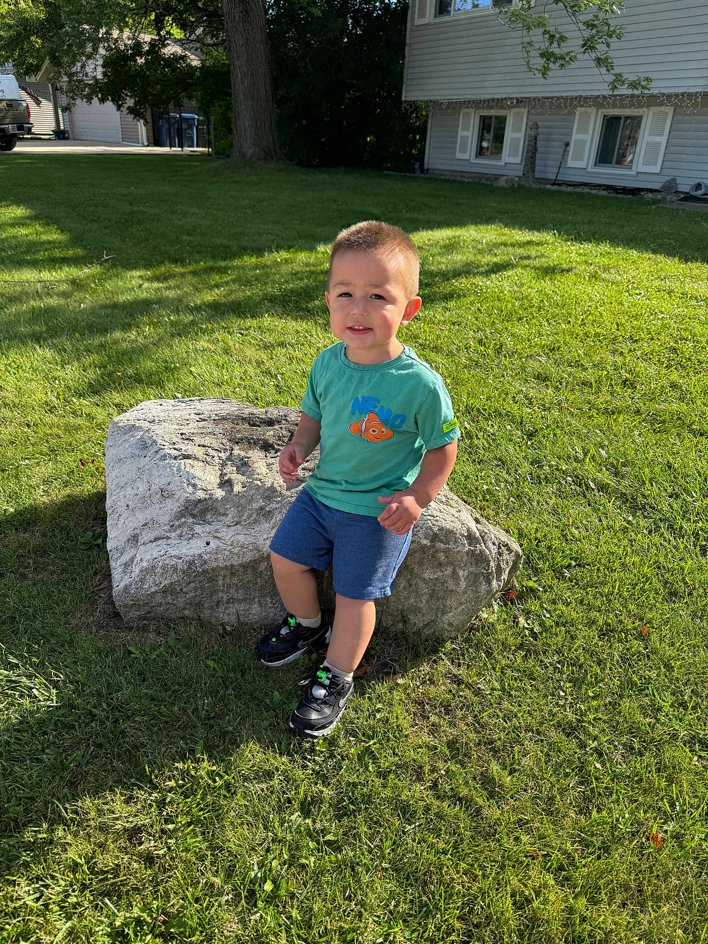 Isaiah joined the competition — help win amazing prizes! toddler, child, boy, rock, grass, tree, sunlight, outdoor, greenery, shorts, tshirt, shoes, sidewalk, house, window, curious, nature, daylight, portrait, playful