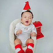 Eliora is registered to the contest to win money with this photo: baby, infant, santa_hat, red_socks, yawning, white_onesie, cozy_seat, decorative_house, holiday_theme, cute, indoor, child, portrait, festive, smiling, soft_texture, holiday_decor, adorable, sitting, young_child